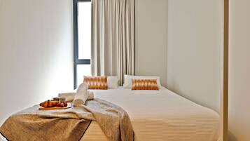 A hotel room with a bed, a window with curtains, a bedside table with a tray of food, and a blanket.