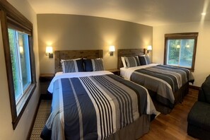 A room with two beds, each with a headboard, bedside lamps, and a window.