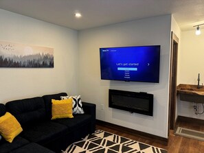Una sala de estar moderna con un televisor de pantalla plana, una chimenea, un sofá con cojines y un cuadro en la pared.