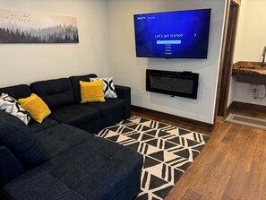 A living room with a dark sofa, patterned rug, and a flat-screen TV mounted on the wall.