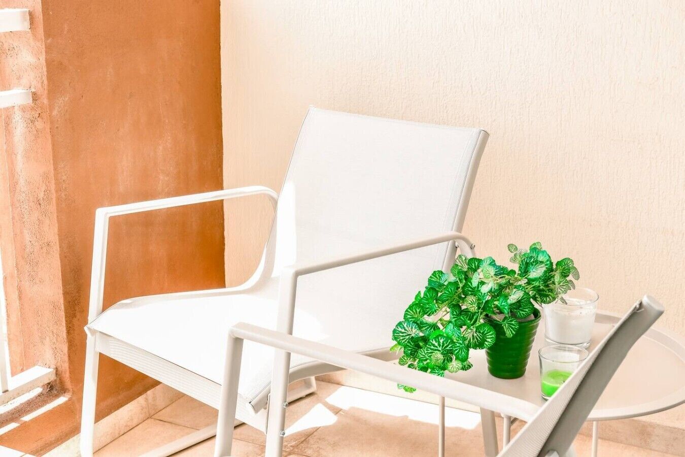 A white chair with a green plant and a glass of water on a table.