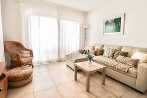 Ein Wohnzimmer mit einer Couch, einem Korbsessel, einem Couchtisch und einem Gemälde an der Wand.