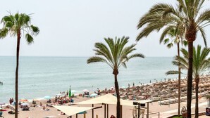 Una playa con palmeras, sombrillas y gente.