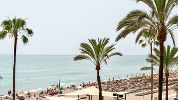 A beach with palm trees, umbrellas, and people.