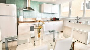 Una cocina moderna con armarios blancos, una mesa de comedor de vidrio y un salpicadero color turquesa.
