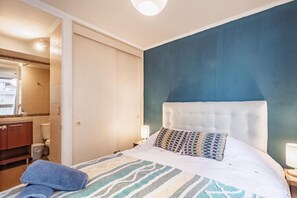 Ein Schlafzimmer mit Bett, Nachttisch, Badezimmer mit Toilette und Spiegel.