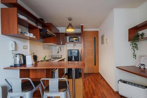 Eine kleine Küche mit Holzschränken, einer Mikrowelle, einem Kühlschrank und einem Waschbecken. Zwei Stühle und ein kleiner Tisch sind vorhanden.