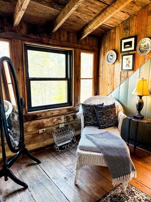 A rustic room with a large window, a wicker chair, a lamp, and wall-mounted plates.