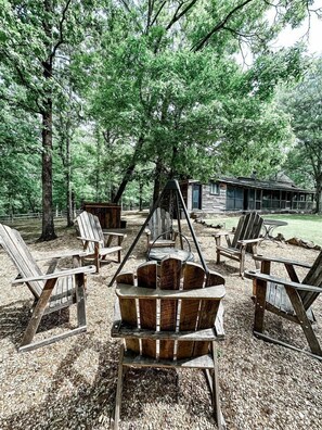 Una cabaña rústica con sillas Adirondack y un brasero en un área boscosa.