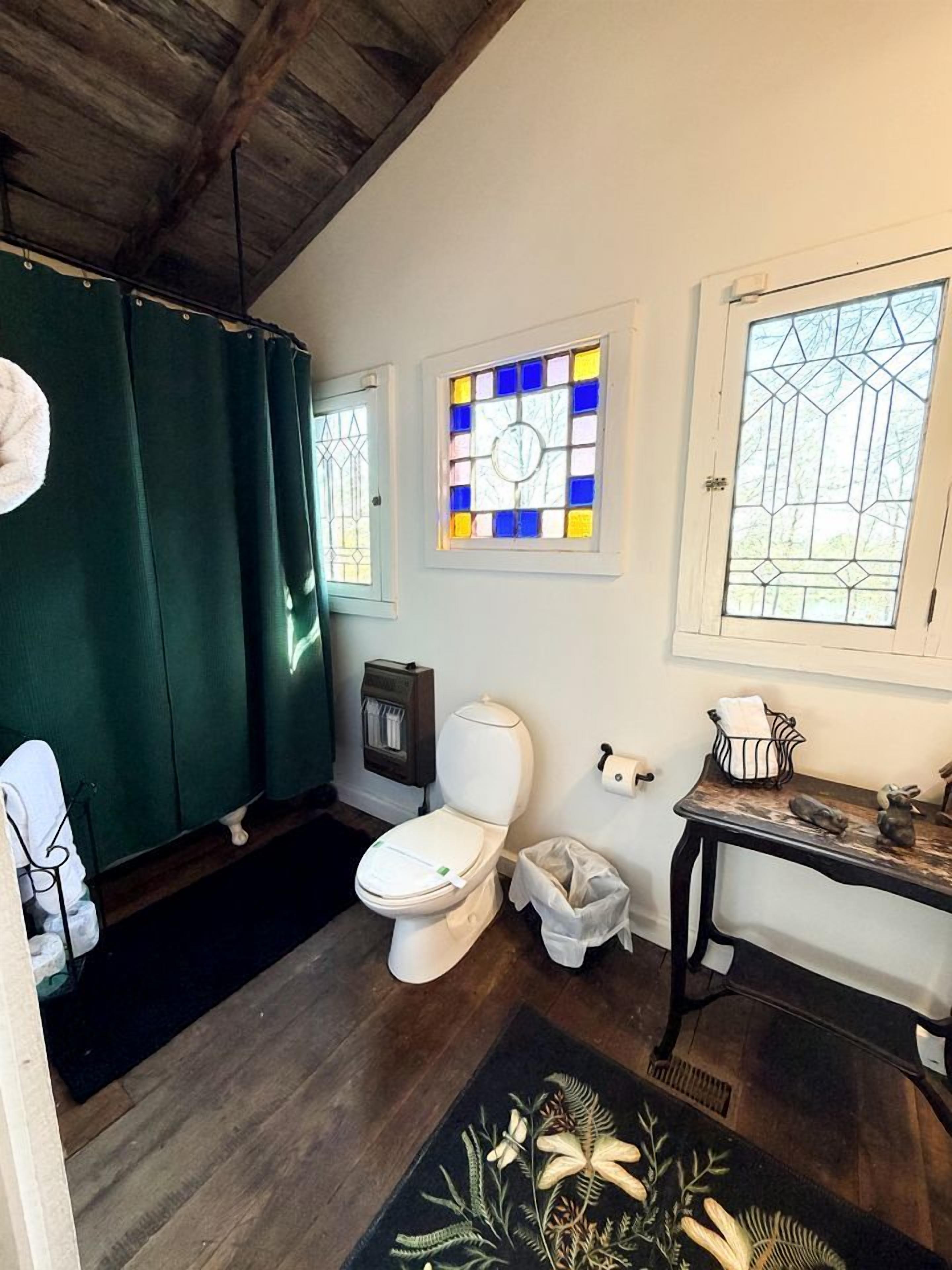 A bathroom with a toilet, a sink, a mirror, a green shower curtain, and a window with stained glass.