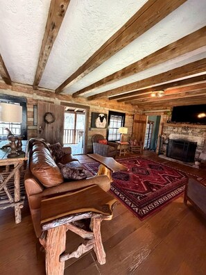 A rustic interior with a wooden ceiling, a fireplace, a leather sofa, and a patterned rug.