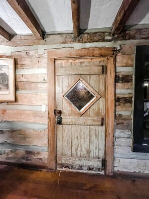 A wooden door with a diamond-shaped window, a framed picture on the wall, and a wooden floor.