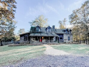 A rustic log cabin with a porch, a chimney, and a gravel driveway.