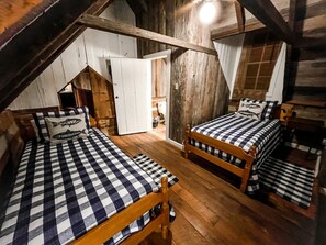 A rustic room with two wooden beds, a wooden wardrobe, and a small white door.