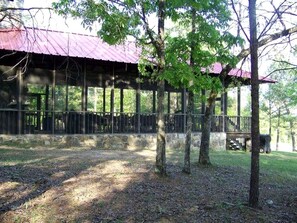Un espace extérieur abrité, doté d’un toit en métal et d’une clôture en bois, et entouré d’arbres.