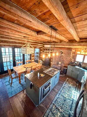 A rustic cabin interior with a wooden dining table, a kitchen island, and a large window.