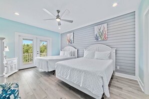 Ein Schlafzimmer mit zwei Betten, einem Deckenventilator, einem Balkon und Blick auf Bäume.