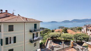 A multi-story building with balconies, a view of the sea, and surrounding greenery.