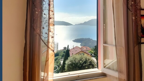 A window with curtains, a view of a body of water, and a distant landscape.