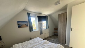 A bedroom with a bed, a window with curtains, a radiator, and a door.