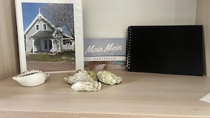 A framed photograph of a house, a black notebook, and some seashells on a shelf.
