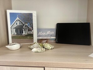 A framed photograph of a house, a black notebook, and some seashells on a shelf.