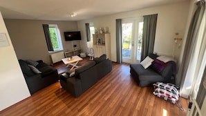 A modern living room with a flat-screen TV, two sofas, a coffee table, and a sliding glass door leading to an outdoor area.