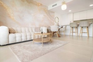 A modern living room with a sofa, a round coffee table, and a dining area with chairs. - Elegant Garden Apartment in Higuerón (Fuengirola)