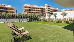 Un patio de hotel con césped cuidado, sillas de descanso y un edificio de varios pisos con balcones.