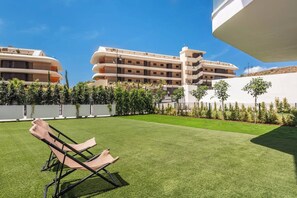 A hotel courtyard with a well-maintained lawn, lounge chairs, and a multi-story building with balconies. - Elegant Garden Apartment in Higuerón (Fuengirola)