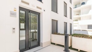 Entrada moderna de un edificio con puerta de cristal, un cartel que indica 'BLOQUE 8 PORTAL 1' y un teclado de seguridad.