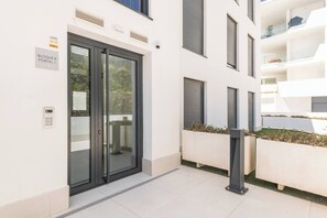A modern building entrance with a glass door, a sign indicating 'BLOQUE 8 PORTAL 1', and a security keypad. - Elegant Garden Apartment in Higuerón (Fuengirola)