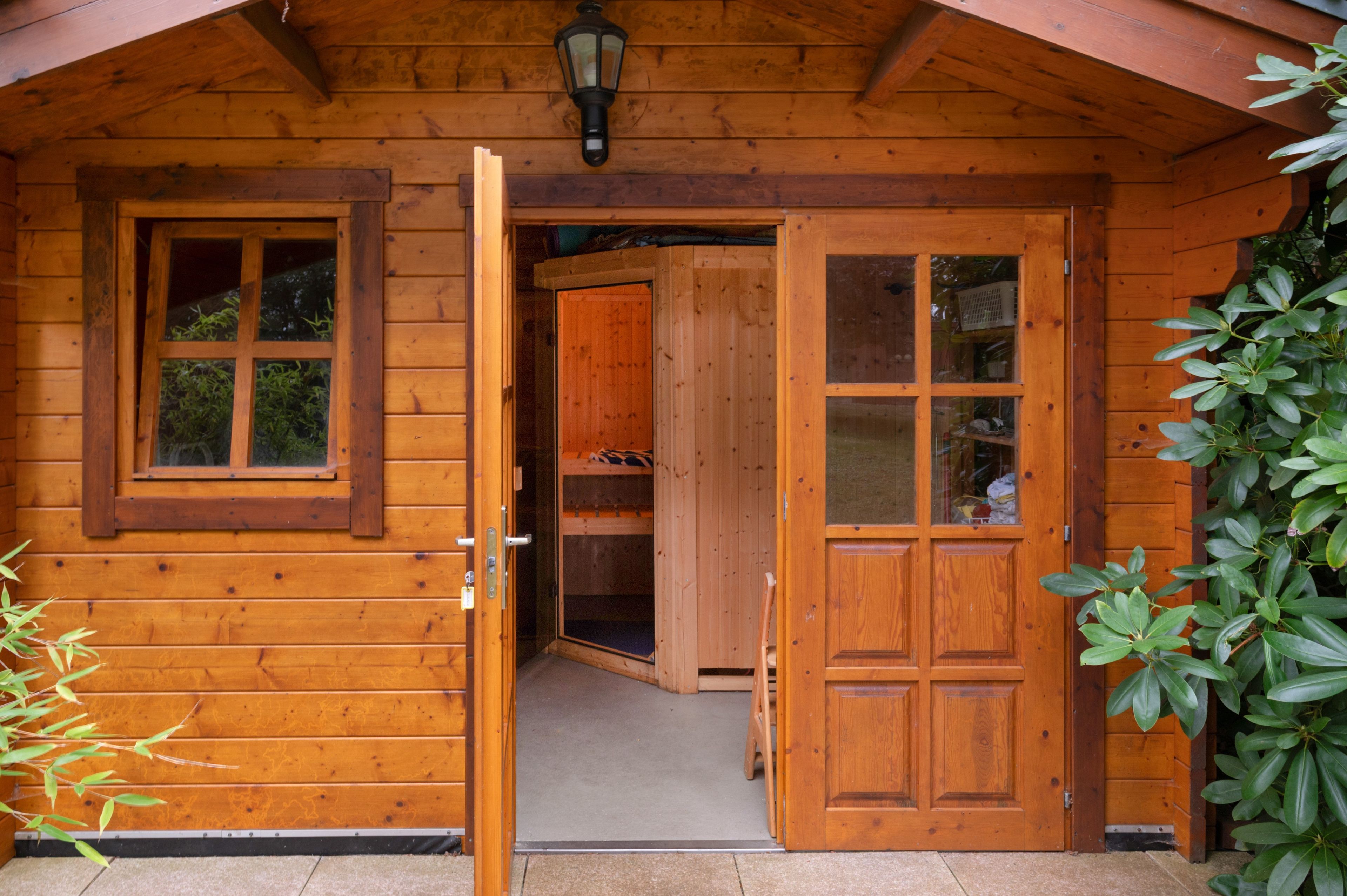 A wooden cabin with a door open to a storage area and a window with blinds.