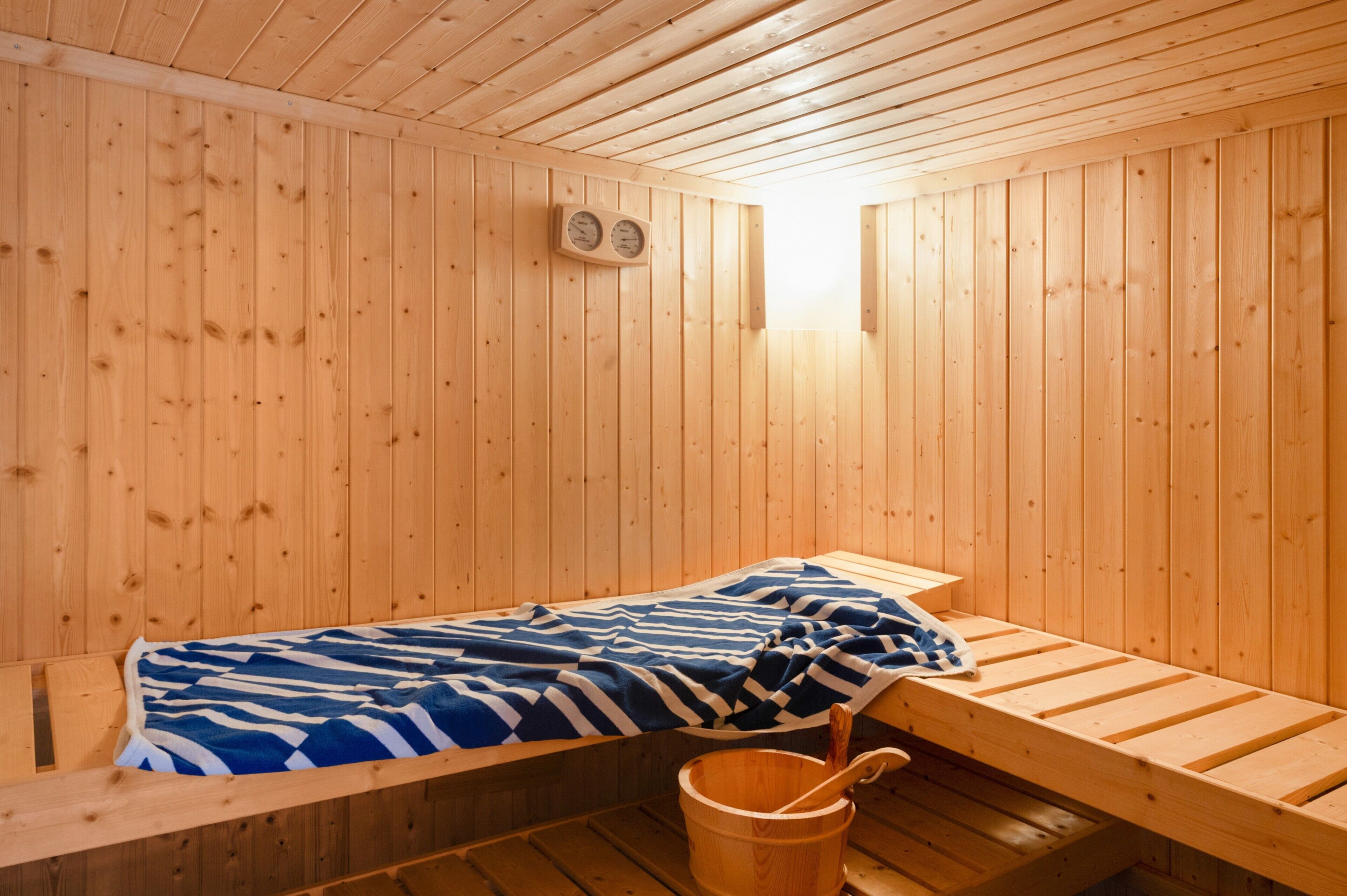 Um salão de sauna de madeira com um banco, um balde e uma toalha.