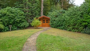 A wooden cabin with a brick pathway leading to it, surrounded by dense greenery. - Holiday Home for 6 Guests in Graal-Müritz (Baltic Sea Spa) (Graal-Müritz)