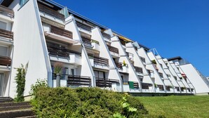 A modern multi-story building with balconies, a grassy area in front, and a clear blue sky. - "Panorama 86" Indoor Pool, Sauna & Separate Bedroom, Near Lake Constance and the Mountains (Scheidegg)