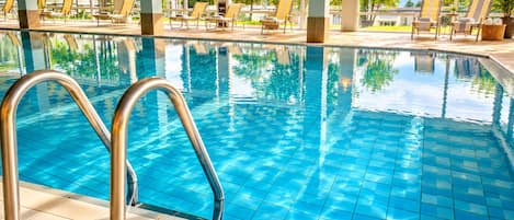 Una piscina con agua cristalina azul, rodeada de sillas de descanso y una terraza con baldosas.