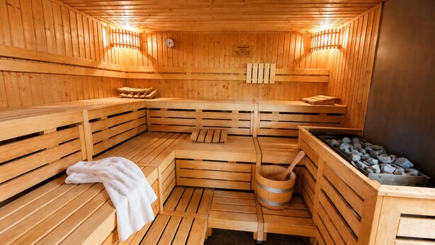 A wooden sauna with benches, a wooden bucket, and a stone-filled container. - "Panorama 86" Indoor Pool, Sauna & Separate Bedroom, Near Lake Constance and the Mountains (Scheidegg)