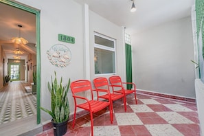 A hallway with a checkered floor, a green door, a number sign, and red chairs.