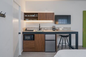 Cocina compacta equipada con microondas, refrigerador, cafetera y taburetes de bar.