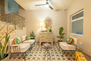 Una habitación con piso a cuadros, un conjunto de sofá, una mesita y un espejo, además de una escalera.
