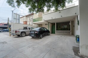 Un edificio moderno con un portón verde, una camioneta pickup blanca y un coche negro estacionados al frente.