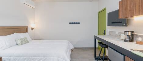 A bedroom with a bed, a ceiling fan, an air conditioner, and a kitchenette with a coffee maker.