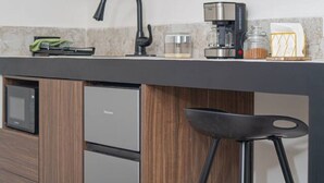 Cozinha moderna com armários de madeira, micro-ondas embutido, geladeira, cafeteira e um banquinho de bar.