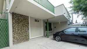 Um edifício moderno com um painel de mosaicos, um portão verde e um carro estacionado em frente.