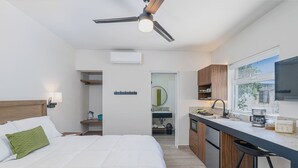 Quarto de hotel com cama, cozinha compacta, ventilador de teto e vista para o exterior.