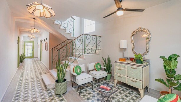A hallway with a checkered floor, a staircase with a decorative railing, a white sofa, a vintage-style dresser, and a ceiling fan.