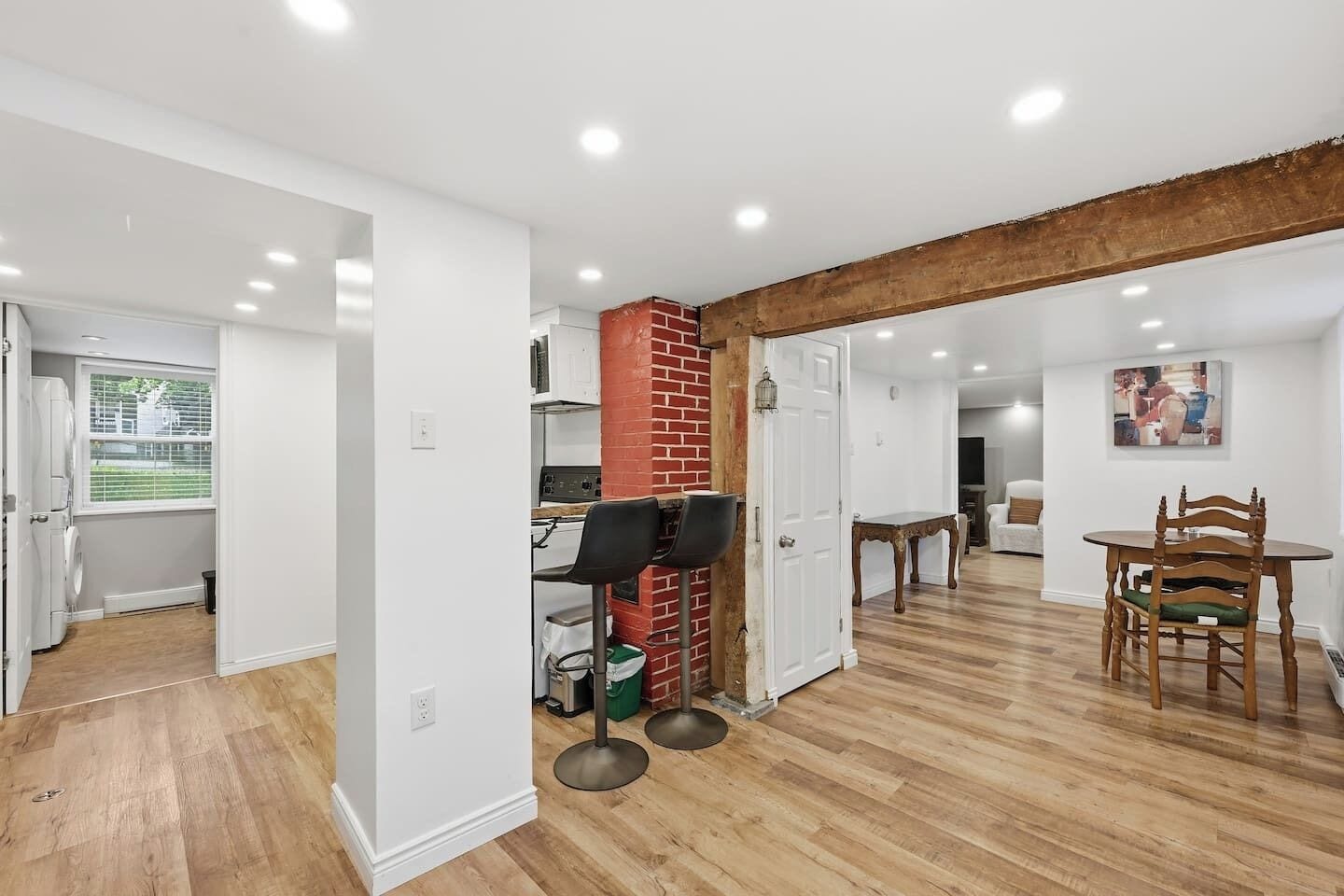 A spacious living area with a kitchen, dining table, and a red brick accent wall.
