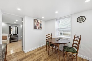 A dining area with a round table, wooden chairs, a painting on the wall, and a clock. - Modern Suite Minutes from Halifax Waterfront (Halifax)