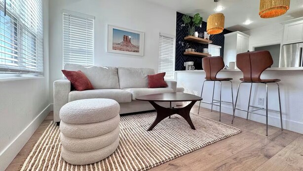 A living room with a sofa, ottoman, coffee table, and bar stools. - Coronado Historic Casita · King Bed · Private Yard · Phoenix (Phoenix)